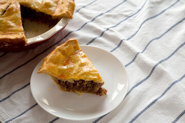 Tasty Homemade Canadian Tourtiere Meat Pie on a white plate, side view. Space for text.