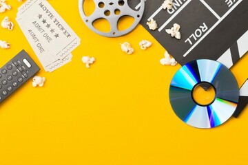 Movie clapper or clapper-board with dvd movie disc, film reel, popcorn, remote control and movie theatre tickets flat lay top view from above on yellow - home cinema or movie night concept - obrazy, fototapety, plakaty