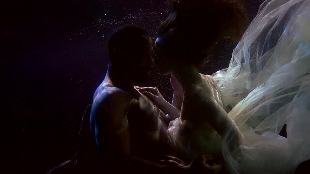 tender caress of young lovers underwater, black man and white woman are floating together