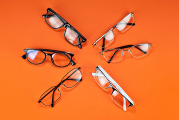 Different types of glasses on an orange background close up. Glasses with rectangular and round frames.