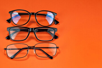 Different types of glasses on an orange background close up. Glasses with rectangular and round frames. Layout for design. Space for text and free space near the object.