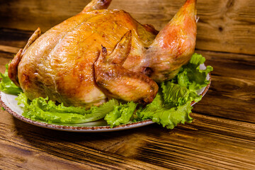 Plate with roasted whole chicken and lettuce leaves on a wooden table
