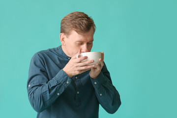 Handsome man with cup of tea on color background