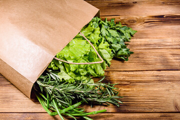 Paper bag with lettuce rosemary and parsley on a wooden table. Vegan food