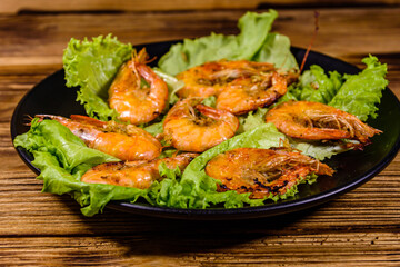 Plate with grilled shrimps and lettuce leaves on a wooden table