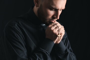 Young priest praying to God on dark background