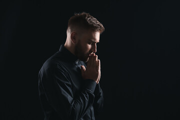 Young priest praying to God on dark background