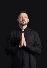 Handsome praying priest on dark background