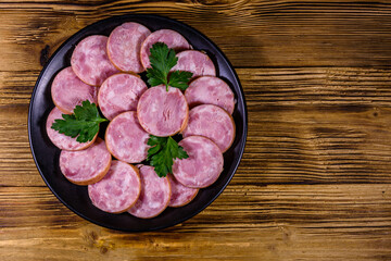 Black plate with sliced sausage on a wooden table. Top view