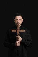 Handsome priest with cross on dark background