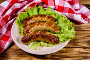 Plate with roasted sausages and lettuce leaves on a wooden table