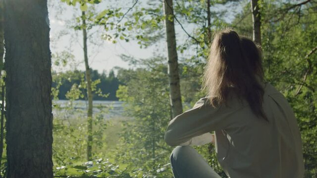 Forest hiker contemplating the view of a lake while taking a break from society, concept of an adventurer in tune with nature