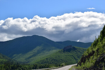 Highway among the hills. White clouds cover the green mountains. Bright summer day.
