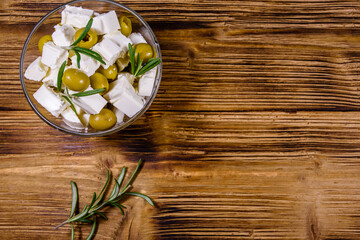 Chopped feta cheese, rosemary and olives in glass bowl on a wooden table. Top view