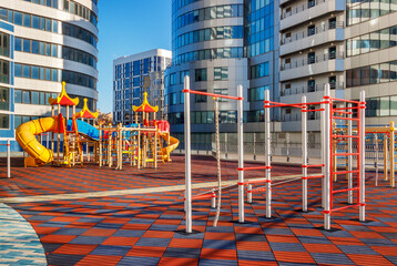 The sunny children's playground among modern futuristic buildings. A luck of natural environment in a city concept