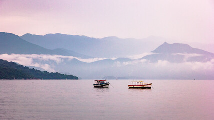 Paraty. Two boats on a vast calm sea. Calm ocean. Morning mist on the mountains surrounding the ocean with two boats.