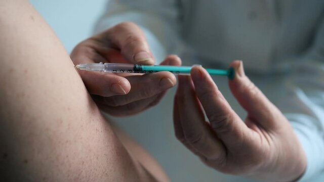 Elderly nurse injects the vaccine for COVID-19 into the arm of a young patient.