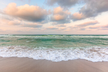 cloudy sunset sea side. waves running the sandy beach. changing windy weather in evening light