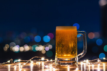A glass of beer on wooden table with colorful city bokeh light background.