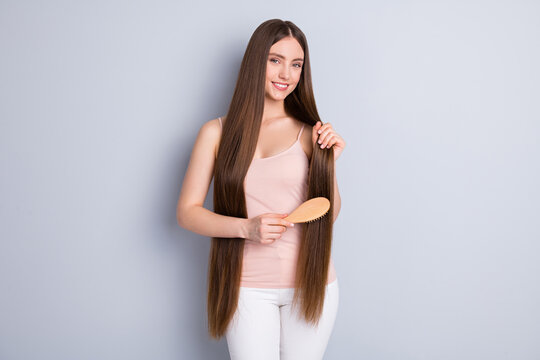 Photo of attractive positive mood lady long hairdo hold wooden comb carefully brushing strong amazing brown curls wear beige singlet isolated grey color background