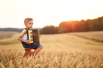 A sad boy plays the accordion. He sitting on a large field of grain.