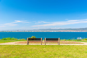 two benches on the sunny beach shore. beautiful view from paved footpath on the seaside. city and mountain in the distance beneath a blue sky with clouds