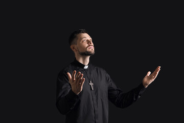 Handsome praying priest on dark background