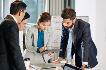 Young Vietnamese businesswoman checking latest news on tablet computer before discussing strategy of work with her team