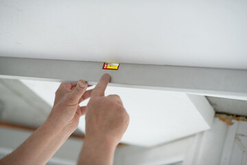 Tool level in men's hands and a flat horizontal surface of the ceiling. Styrofoam, seiling...