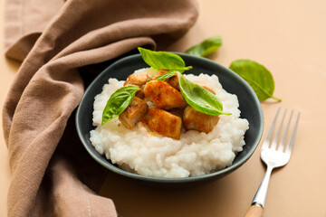 Bowl with boiled rice and chicken on color background