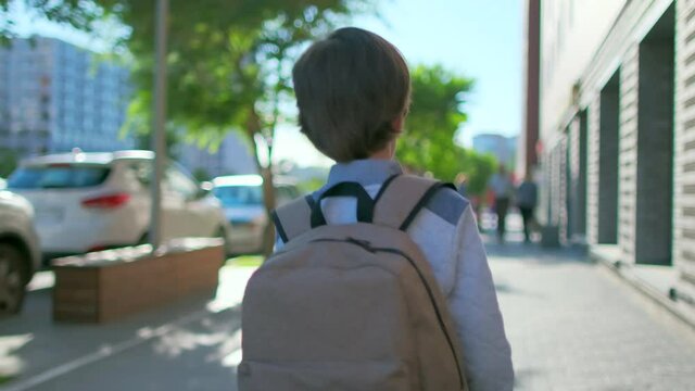 Schoolboy Little boy child with backpack alone going to school at sunset street outdoors. Back view. First-grade student, primary school, first grader, first class education, 4 K slow-mo