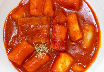 Spicy korean dish topokki of rice dumplings on white plate close up top view.