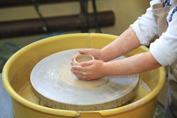 Fototapeta premium Children's hands create a clay product on a pottery wheel in a pottery workshop. Education hobbies, art, craft
