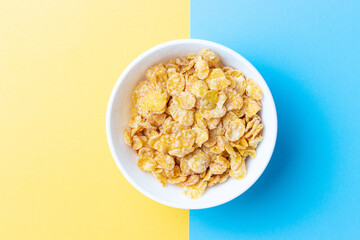 Plate with breakfast cereal on blue and yellow background, view from above