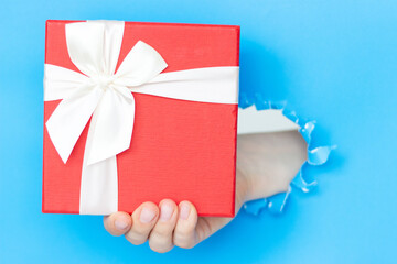 A woman's hand holds a gift with a white bow on blue background