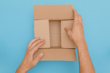 Hands fold empty cardboard box ready to deliver as package on blue background