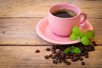 Closeup pink cup of black coffee with fresh green mint ( peppermint ) leaves and coffee beans isolated on rustic wooden table background.