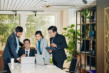 Business people gathered at laptop of coworker to discuss figures in his report