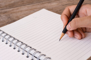 Mockup woman hand  writing by black pencil on blank notebook isolated on white background .