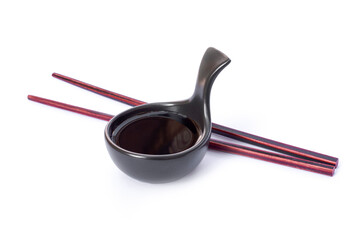 Tasty soy sauce in small black ceramic bowl and red chopsticks isolated on white background.