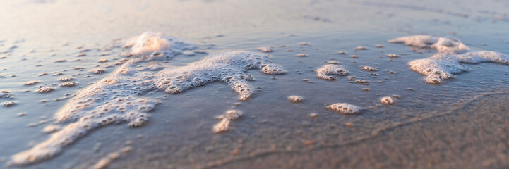 sea foam on the shore, sunset on the background, blurry background