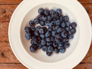 Blueberry is on the white plate. Blueberry on the wood