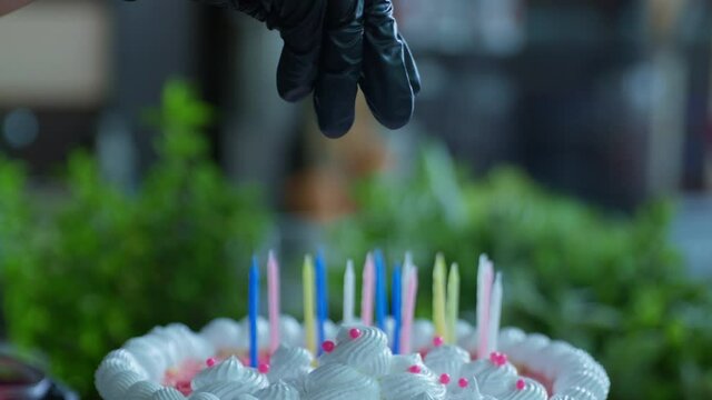 close-up, chef in gloves sprinkles sweet decorations on cake with candles for celebration and congratulations birthday in cafe or restaurant