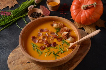 Creamy pumpkin and sweet potato (batata) soup with bacon on dark background.A bowl of the soup with homemade croutons and herbs with autumn decorations.