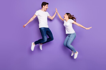 Plakat Full length profile side photo of cheerful two people freelancer jump win discount clap high five gesture wear white t-shirt denim jeans gumshoes isolated over violet color background