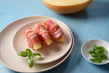 Summer appetizer with sweet melon and ham on blue background