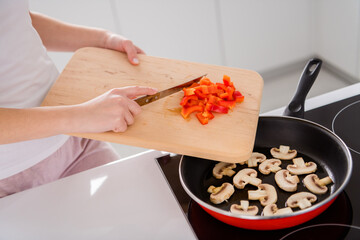 Cropped top above high angle view photo of tasty ecological supper preparation woman add chopped fresh pepper frying pan mushroom in house kitchen indoors
