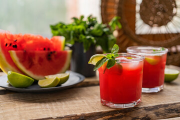 Watermelon smoothie lemonade with lime, topping with fresh mint leaves for the summer drinks concept. Homemade refreshing cold drink on wooden rustic table near window. Selective focus, copy space.