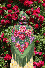 Blossoming bush: roses in summer garden. Seasonal red flowers. Russian girl in traditional national folk Pavlovo Posad shawl, vintage Pavloposadsky, Pavlovoposadsky scarf. Girl in Suzdal town, Russia