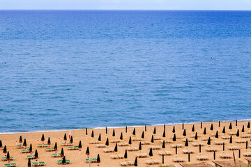 view of  a blue sea and a beach equipped with closed umbrellas in Italy